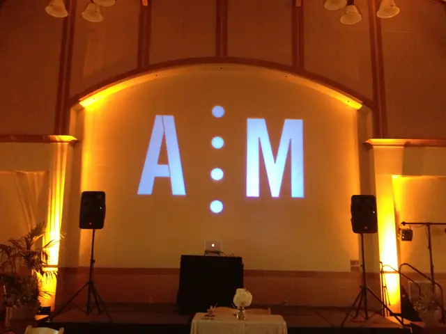 A couple's monogram projected on the stage wall with amber uplighting and the DJ booth at Mill Valley Community Center in Mill Valley