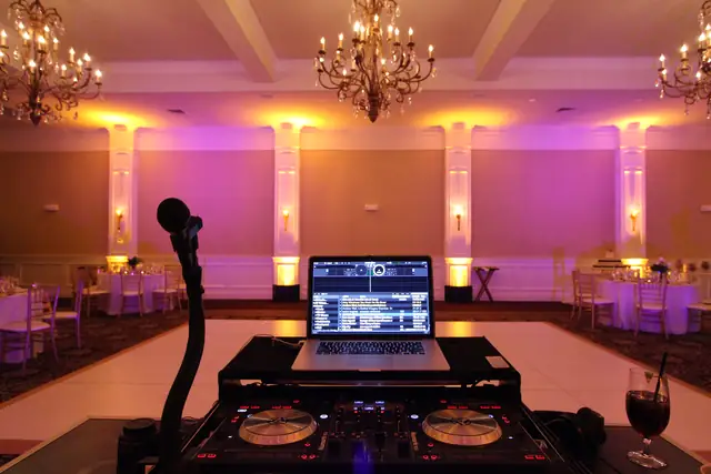 DJ controller, laptop and microphone set up facing the ballroom at Oceano Hotel and Spa, with purple and amber uplighting and chandeliers