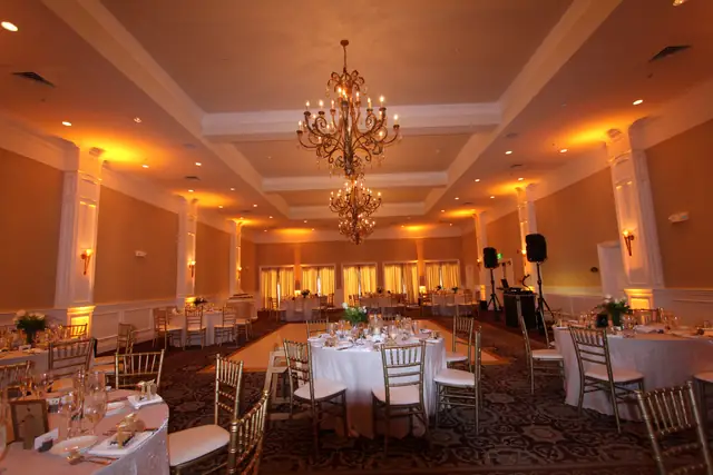 Oceano Hotel and Spa ballroom set for dinner with amber uplighting, gold chairs and a DJ setup on the right wall