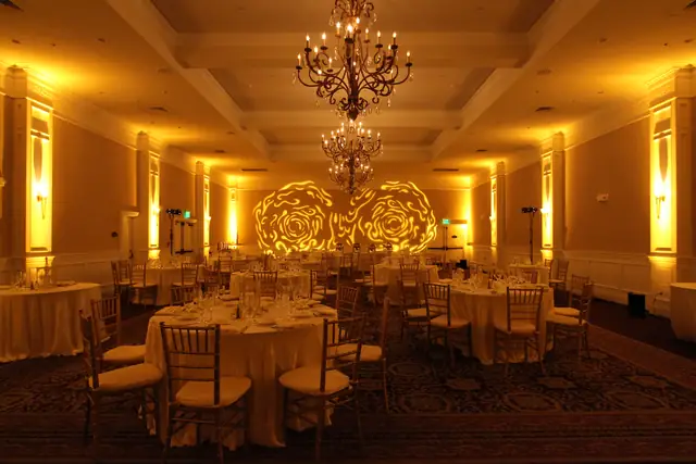 Oceano Hotel and Spa ballroom lit amber with rose pattern projections on the wall behind set dinner tables