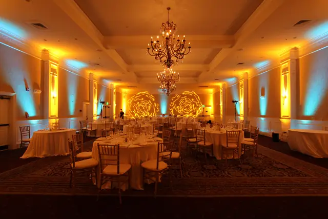 Banquet room at Oceano Hotel and Spa with chandeliers, set tables, gold and aqua uplighting and two rose gobos on the far wall