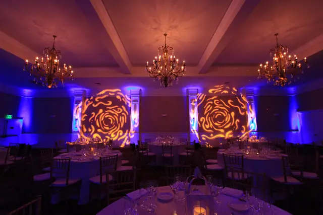 Oceano Hotel and Spa banquet room with three chandeliers, set tables, blue uplighting and two rose pattern gobos on the wall