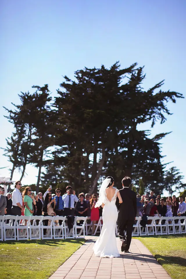 A bride walks up the aisle at an outdoor ceremony under cypress trees at Oceano Hotel and Spa, Half Moon Bay