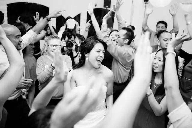 A bride laughs in the middle of a crowded dance floor, guests' hands raised around her, at a wedding at Oceano Hotel and Spa, Half Moon Bay