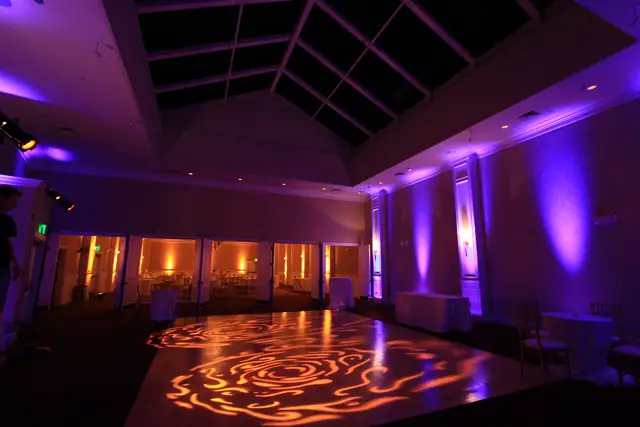 Atrium dance floor at Oceano Hotel and Spa with lavender uplighting and a rose pattern projected on the floor, with the ballroom visible through open doors