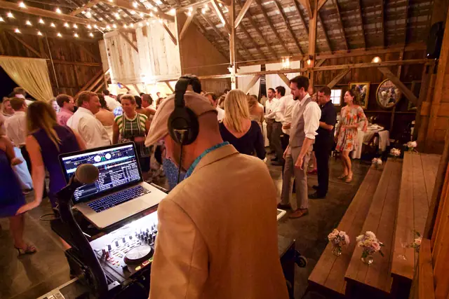Wayne at his DJ setup with headphones on, facing a crowd on the barn floor at Olympia's Valley Estate