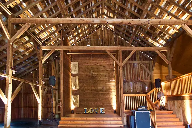 Timber-framed barn interior at Olympia's Valley Estate with a raised platform, LOVE marquee letters, speakers on stands and the DJ booth beside the stairs