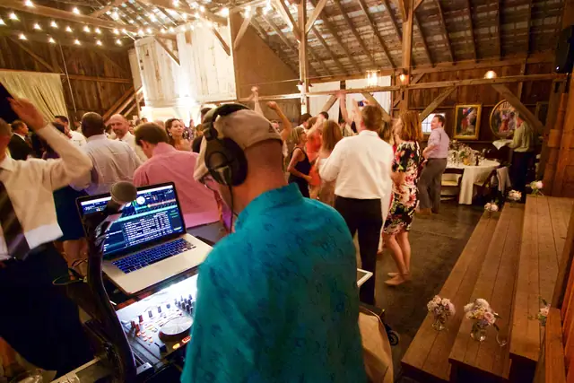 Guests dancing on the barn floor at Olympia's Valley Estate while Wayne works at his laptop and controller