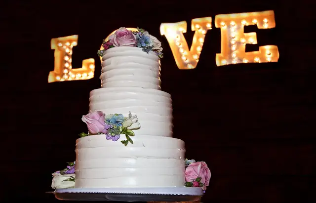 Wedding cake with fresh flowers in front of lit LOVE marquee letters in the barn at Olympia's Valley Estate