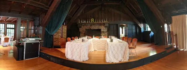 Wide view of the Mill Valley Outdoor Art Club hall with fireplace, stage tables and a DJ booth with speakers on both sides