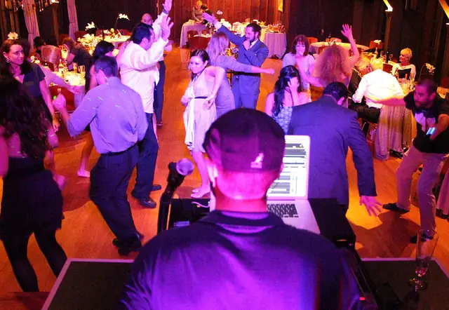 Guests dancing across the wood floor of the Outdoor Art Club in Mill Valley, seen from behind the DJ booth