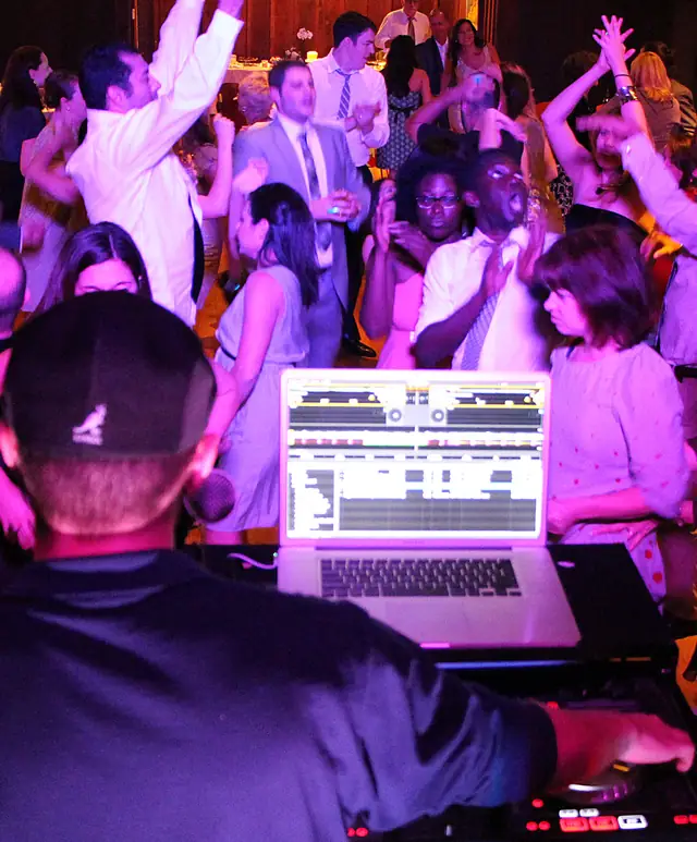 Guests singing and dancing with arms raised at an Outdoor Art Club reception in Mill Valley, seen over the DJ's shoulder
