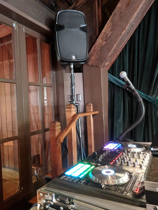 DJ controller with glowing pads and a microphone beside a speaker and wood railing at the Mill Valley Outdoor Art Club