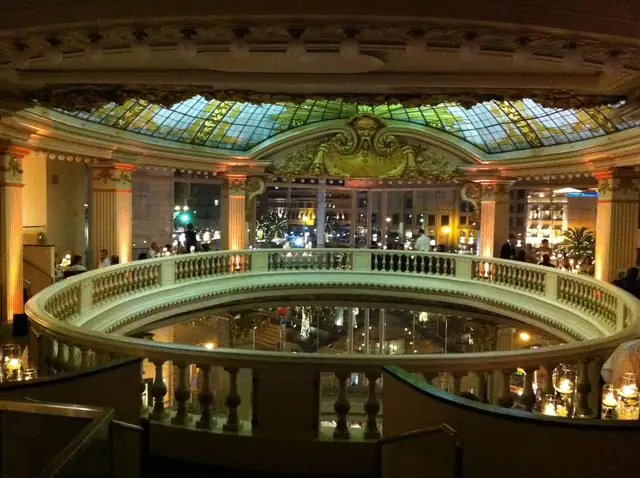 Night view of the Rotunda at Neiman Marcus in San Francisco, with a stained glass dome, columns lit in amber and a curved balustrade overlooking the room