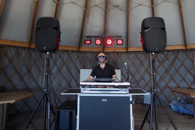 DJ Wayne Noel smiling at his booth with two speakers and red lights inside the yurt at Slide Ranch, Muir Beach