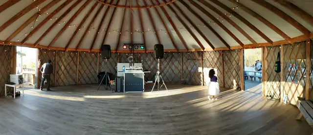 DJ booth with two speakers set up inside the string-lit yurt at Slide Ranch, with warm light across the wood floor