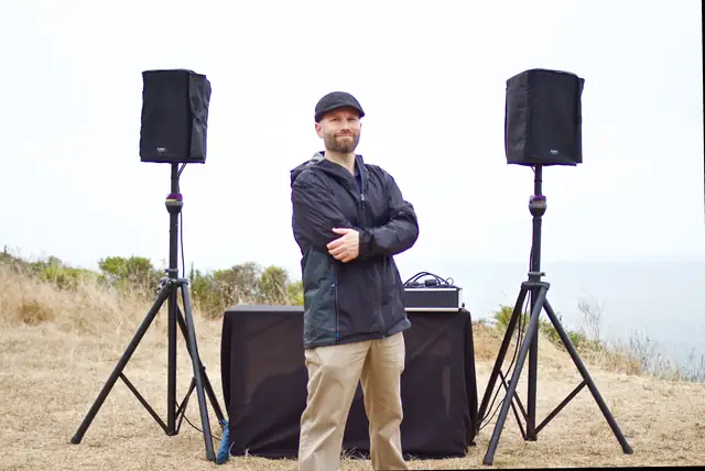 DJ Wayne Noel standing between two speakers at his outdoor booth on the bluff at Slide Ranch