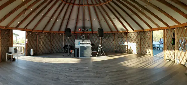 Panorama of the yurt interior at Slide Ranch with string lights, wood floor and DJ setup