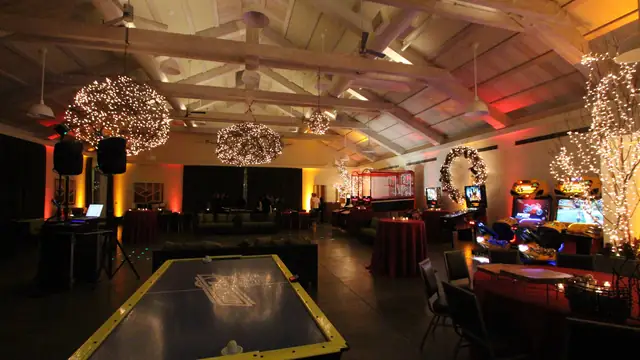 DJ booth and speakers beside arcade games and lit trees at a holiday party at Solage, Calistoga