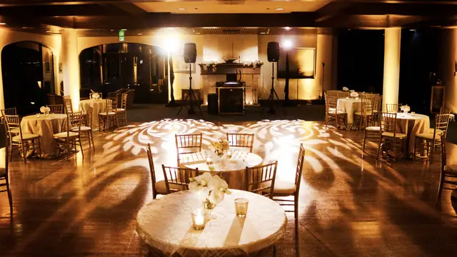 St. Francis Yacht Club event room at night with gold uplighting, a patterned dance floor and a DJ setup in front of the fireplace