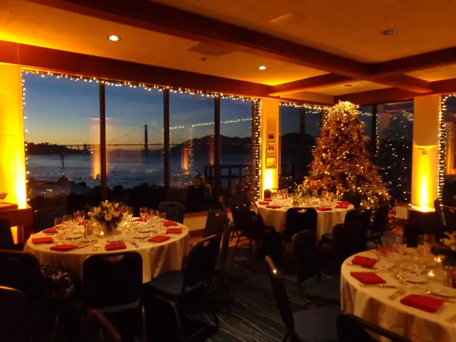 Dinner tables set beside bay windows with a view of the Golden Gate Bridge at dusk inside St. Francis Yacht Club