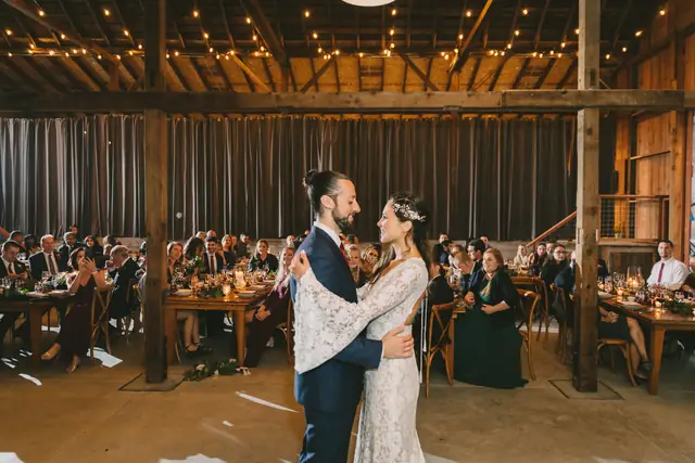 A couple's first dance in the barn at Straus Home Ranch in Marshall, with guests watching from long farm tables under string lights