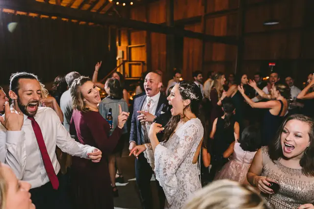 Bride, groom and guests singing along on a packed dance floor in the barn at Straus Home Ranch in Marshall