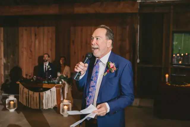 A wedding toast on a wireless microphone in the barn at Straus Home Ranch in Marshall, the couple listening from their sweetheart table