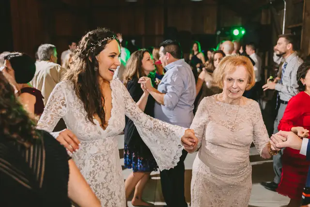 A bride dancing hand in hand with an older family member on the dance floor in the barn at Straus Home Ranch in Marshall