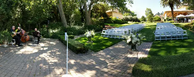Ceremony garden at The Madrona in Healdsburg with a brick terrace, a hedge, live strings and rows of white chairs on the lawn