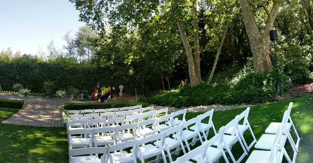 Ceremony chairs on a lawn at The Madrona with a speaker on a stand beneath tall shade trees