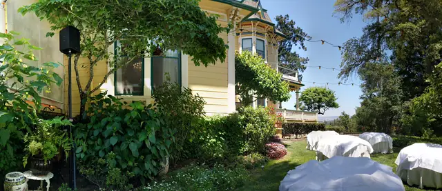Victorian mansion at The Madrona with string lights over the garden, a speaker on a stand among the plants and covered tables on the lawn beyond