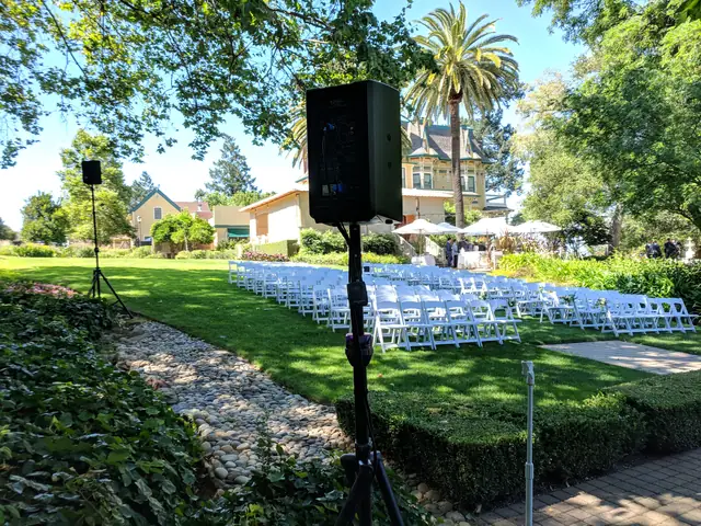 Speakers set up for an outdoor ceremony at The Madrona with white chairs on the lawn, a palm tree and the mansion beyond