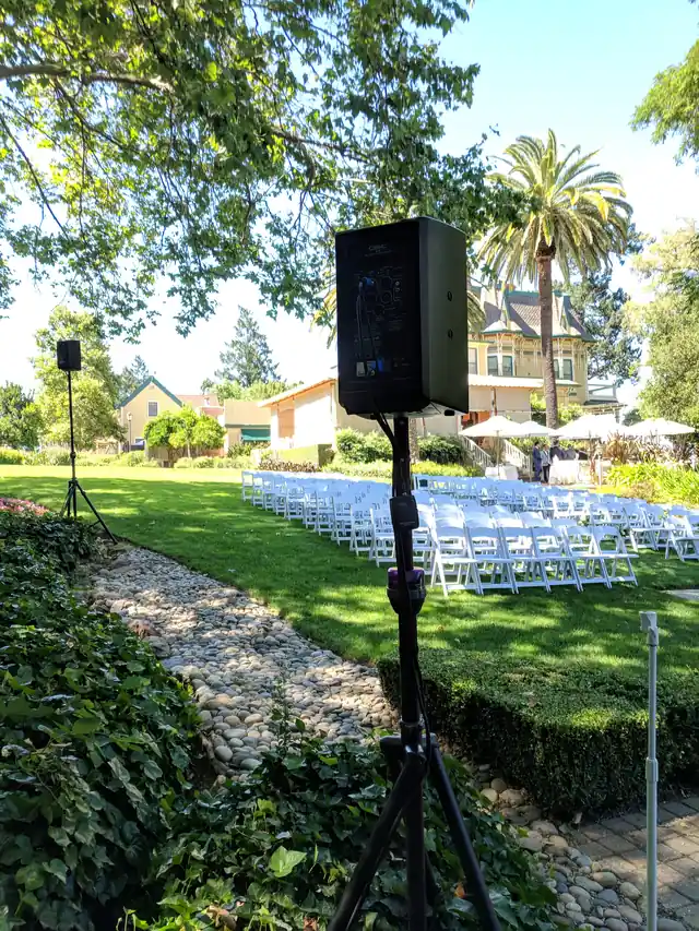 Speaker on a stand beside ceremony chairs at The Madrona with a palm tree and the mansion in the background