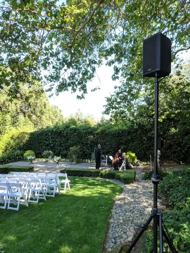 Ceremony garden at The Madrona with a speaker on a stand, white chairs and a hedge-backed terrace with live strings