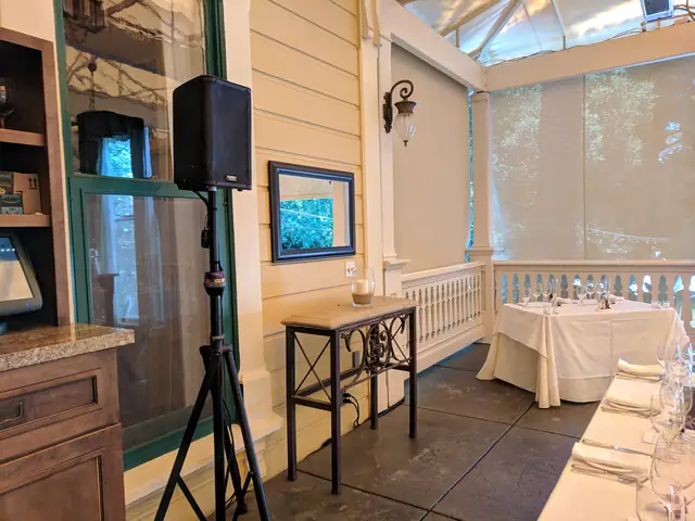 Speaker on a stand in the corner of a covered porch at The Madrona beside a wooden hutch and a wall screen