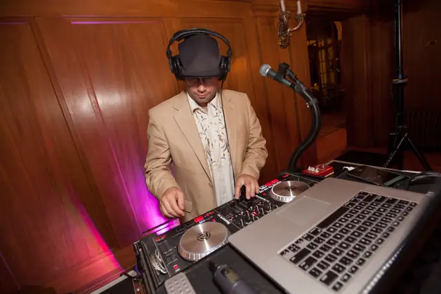 DJ Wayne Noel at his controller in the wood-paneled ballroom at Villa Montalvo with pink uplighting on the wall