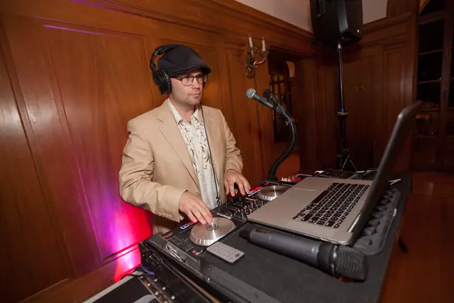 DJ Wayne Noel mixing with a speaker on a stand beside him in the paneled ballroom at Villa Montalvo