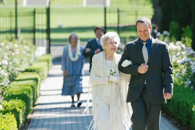 Family members walk arm in arm down the rose-lined garden path during a wedding processional at Villa Montalvo in Saratoga