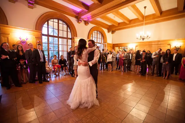 A couple's first dance on the parquet floor of the wood-paneled hall at Villa Montalvo in Saratoga, ringed by guests