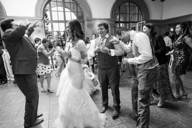 Black and white photo of a bride, groom and guests laughing and dancing in the hall at Villa Montalvo in Saratoga