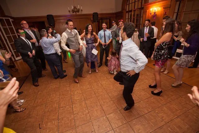 Guests dancing in a circle on the parquet floor of the hall at Villa Montalvo in Saratoga, with two speakers on stands behind them