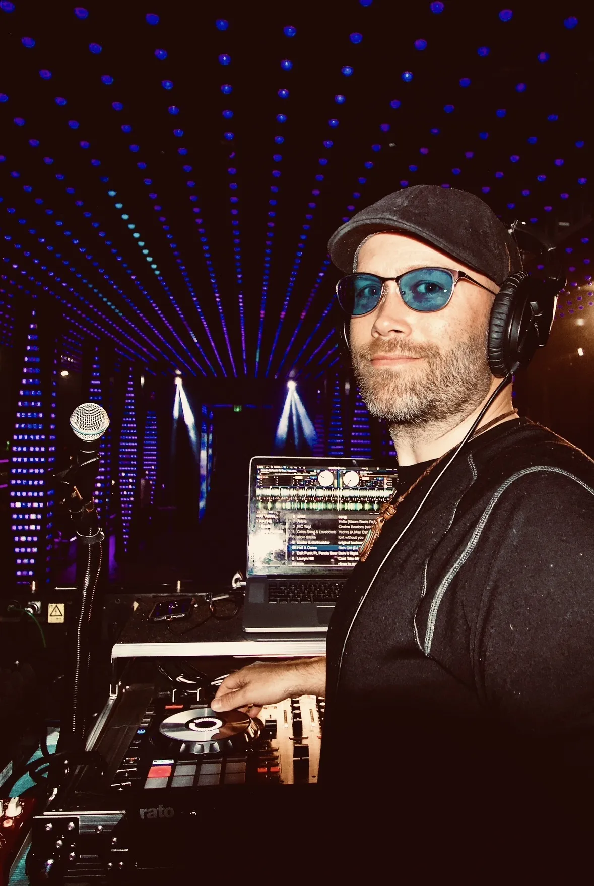 DJ Wayne Noel behind the decks at a club, headphones on, mixing live